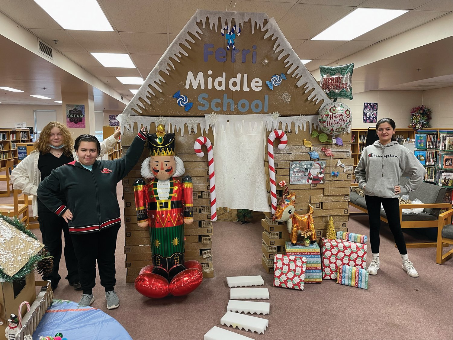 GINGERBREAD GENIUSES: Saylor Pizzi, Katelyn Silva, and Harliey Jimenez pose with the giant gingerbread house they helped build in the Ferri Middle School library.